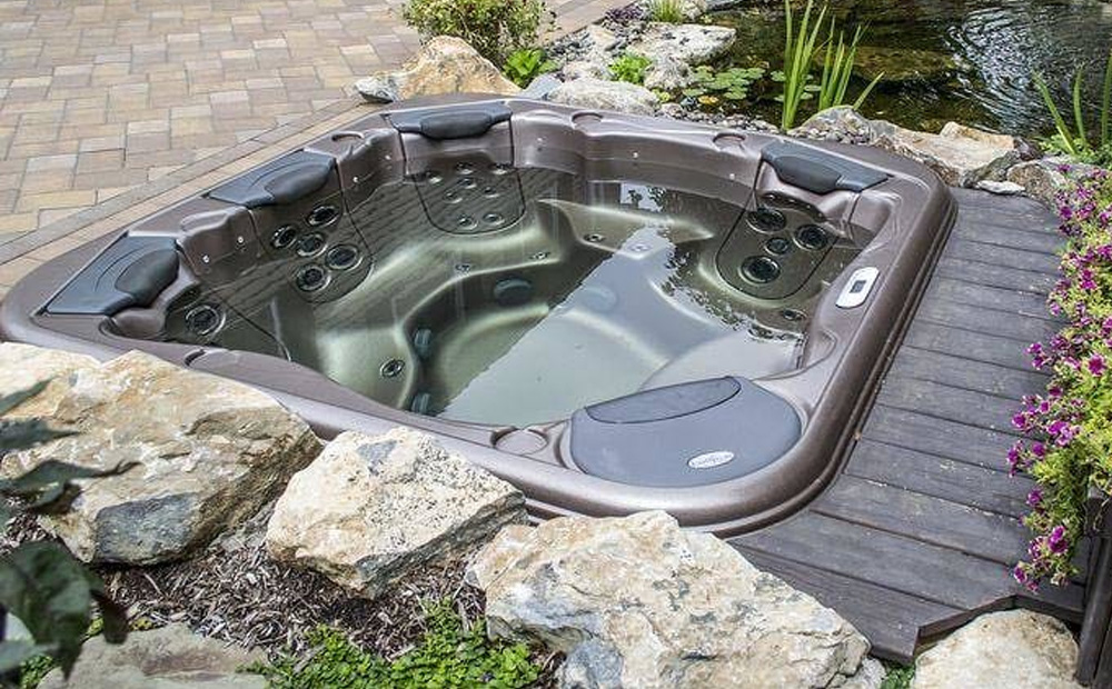 Outdoor hot tub recessed into a landscaped patio with natural stone, wooden decking, and garden plants.
